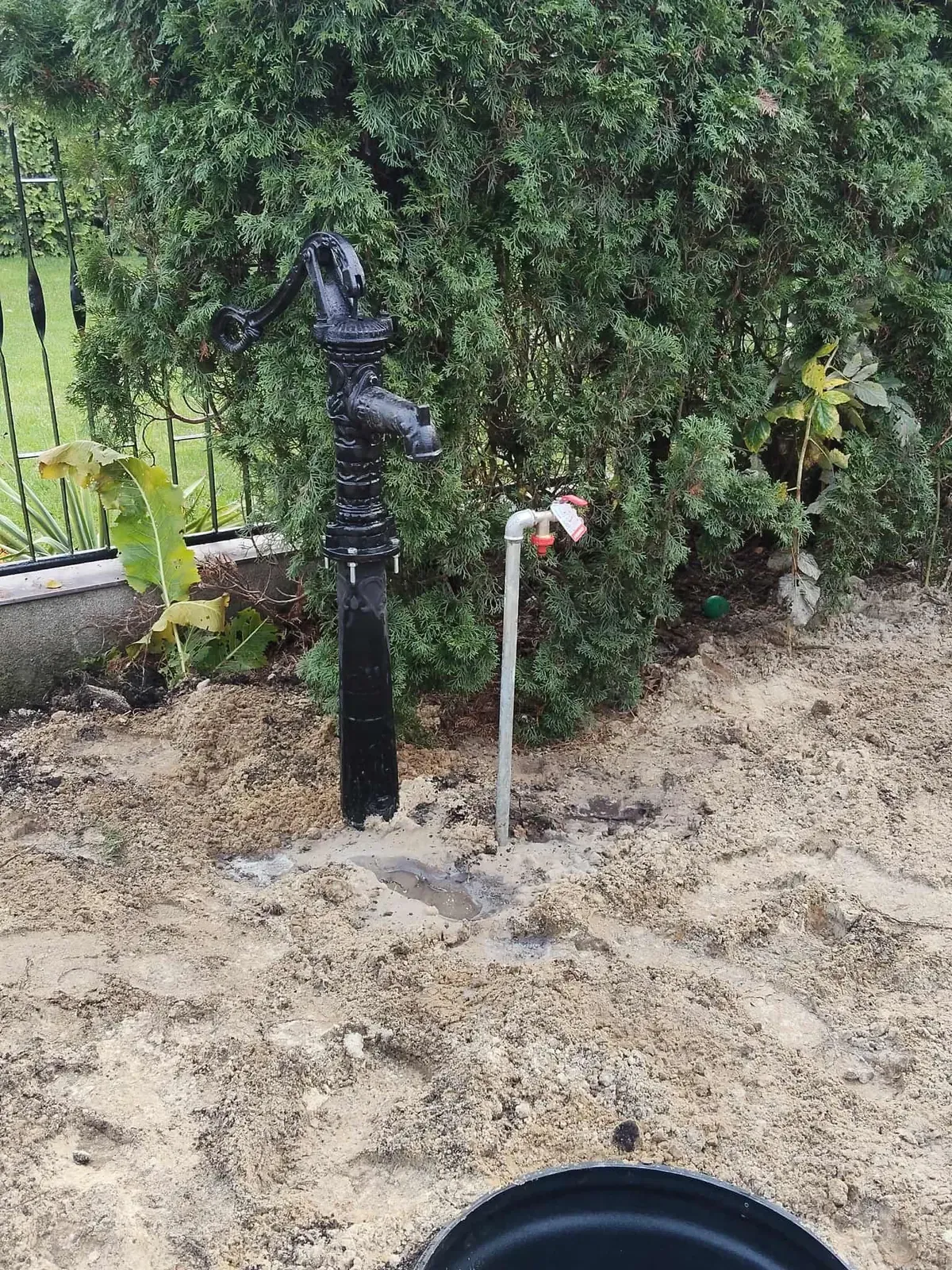 Czarna pompa ręczna i kran ogrodowy przy studni w ogrodzie